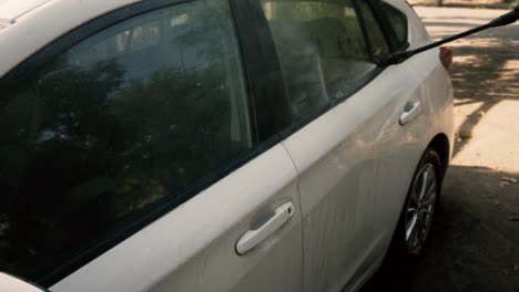 male cleaning a white car with a pressure washer