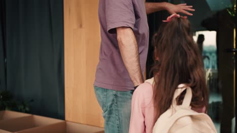 un hombre con cabello gris en una camiseta púrpura recoge a su hija en un vestido rosa y con una mochila blanca de un grupo para preparar a los preescolares para la escuela