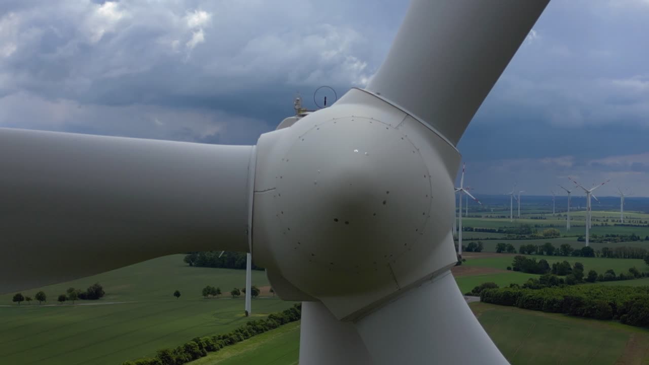 Wind turbines generating clean energy in a large wind park in Germany, under a cloudy sky. close up Great aerial view flight fly push forward drone