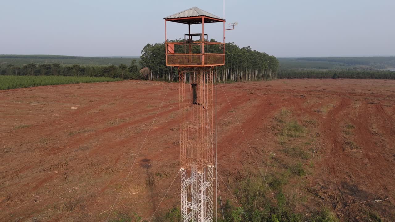 A drone ascends over a forest guard tower placed in a reforestation field, showcasing the vast landscape and ongoing environmental protection efforts.