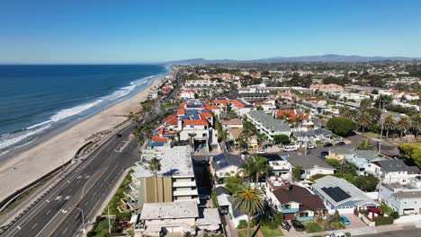 aerial shot from right to left over the beautiful beach of carlsbad california, usa and coast highway with cars passing by beside the beach on a town landscape