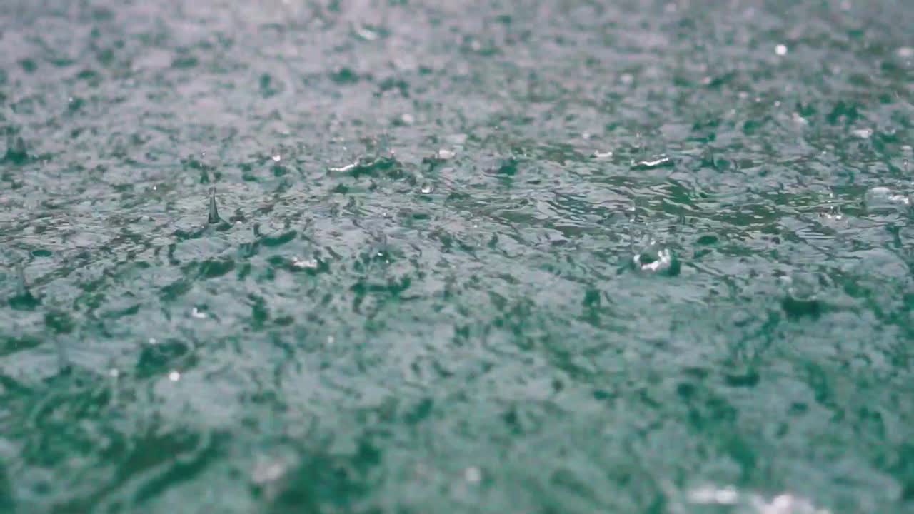 Slow motion heavy rainfall hitting surface of swimming pool