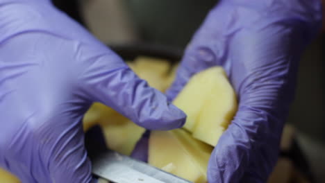 close up of hands with purple gloves cutting russet potato with knife