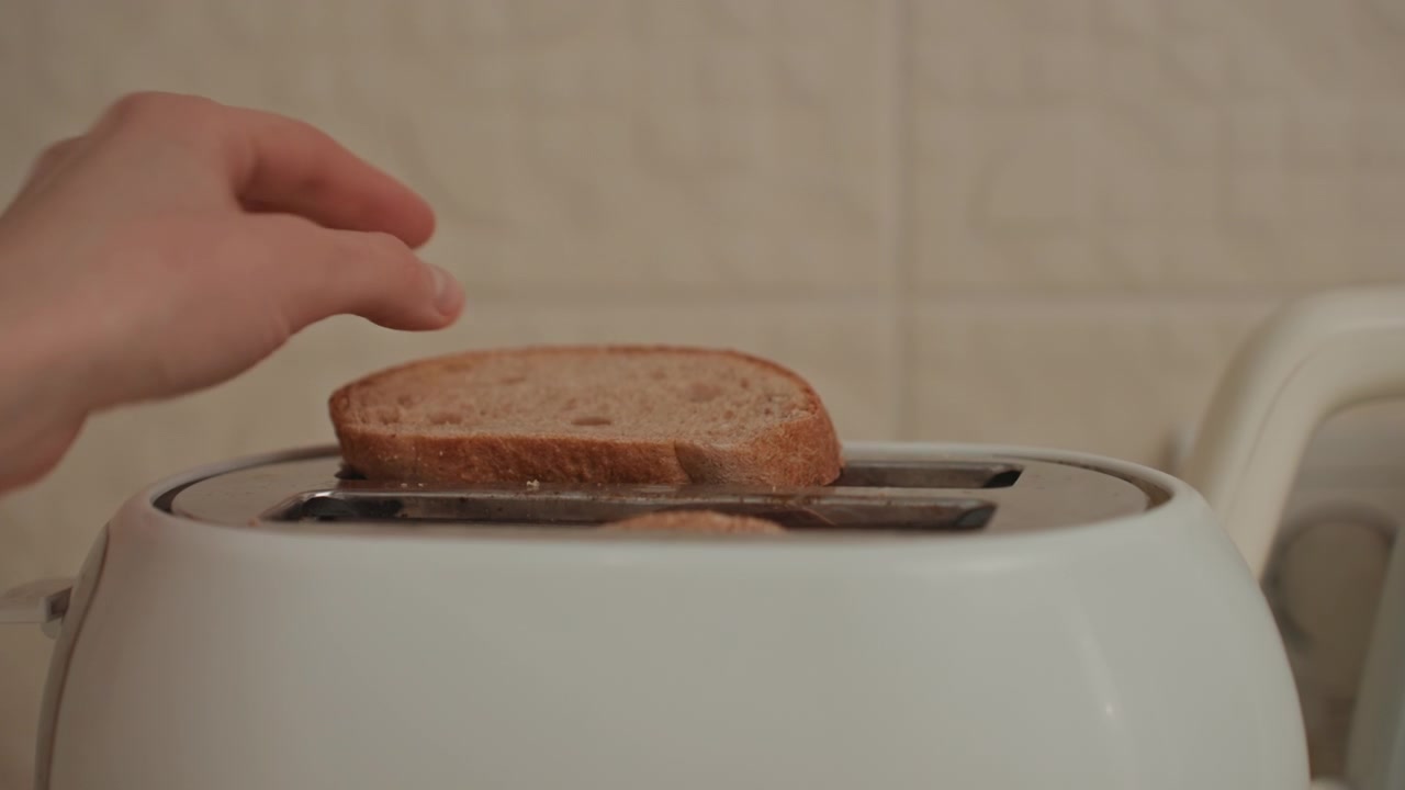 Hand places bread into toaster, intimate gesture of morning routine, fingers adjust slice, gentle rhythm, music lover preparing breakfast, soft light, closeup on crust and crumb, domestic warmth
