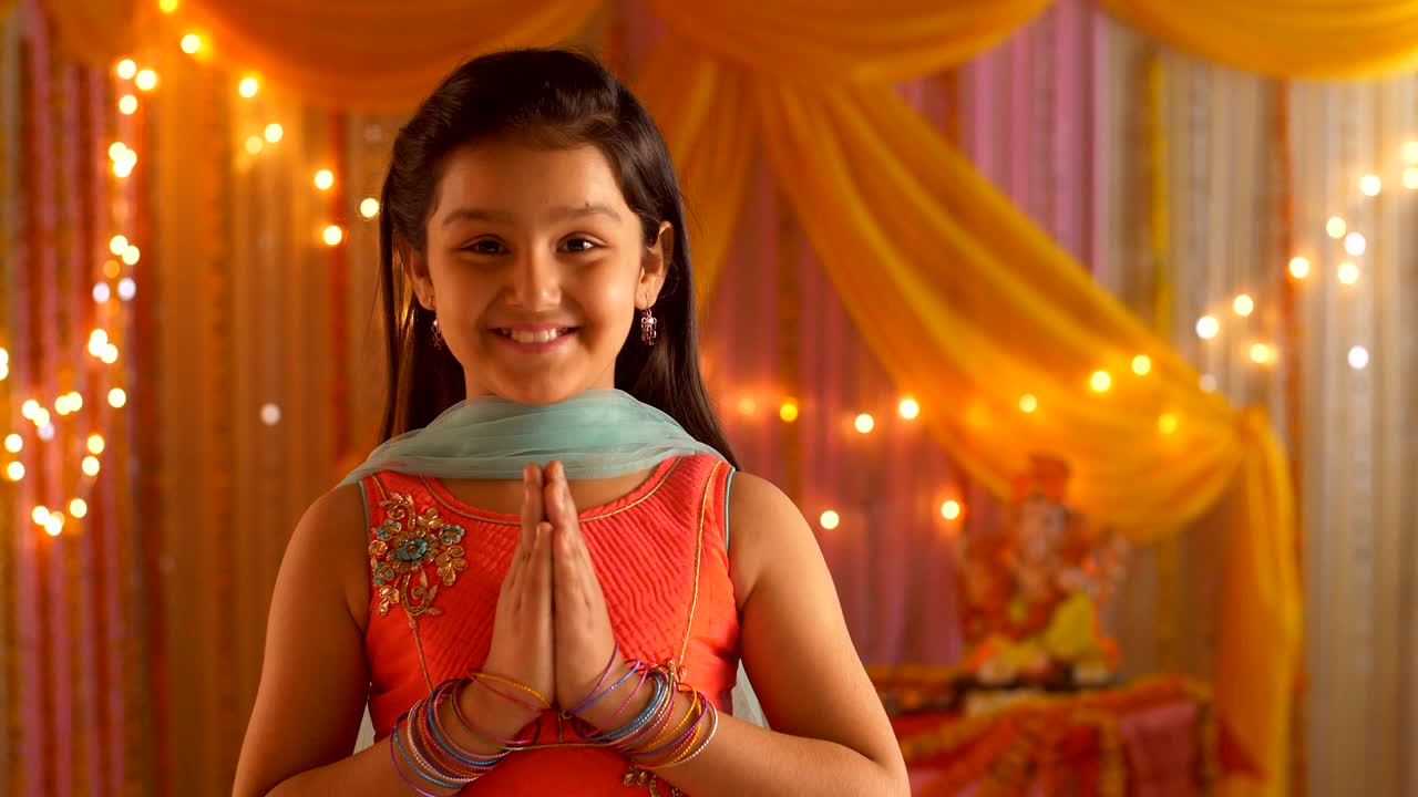 Indian girl child folding hands in namaskar form and looking in the camera - Festive Background