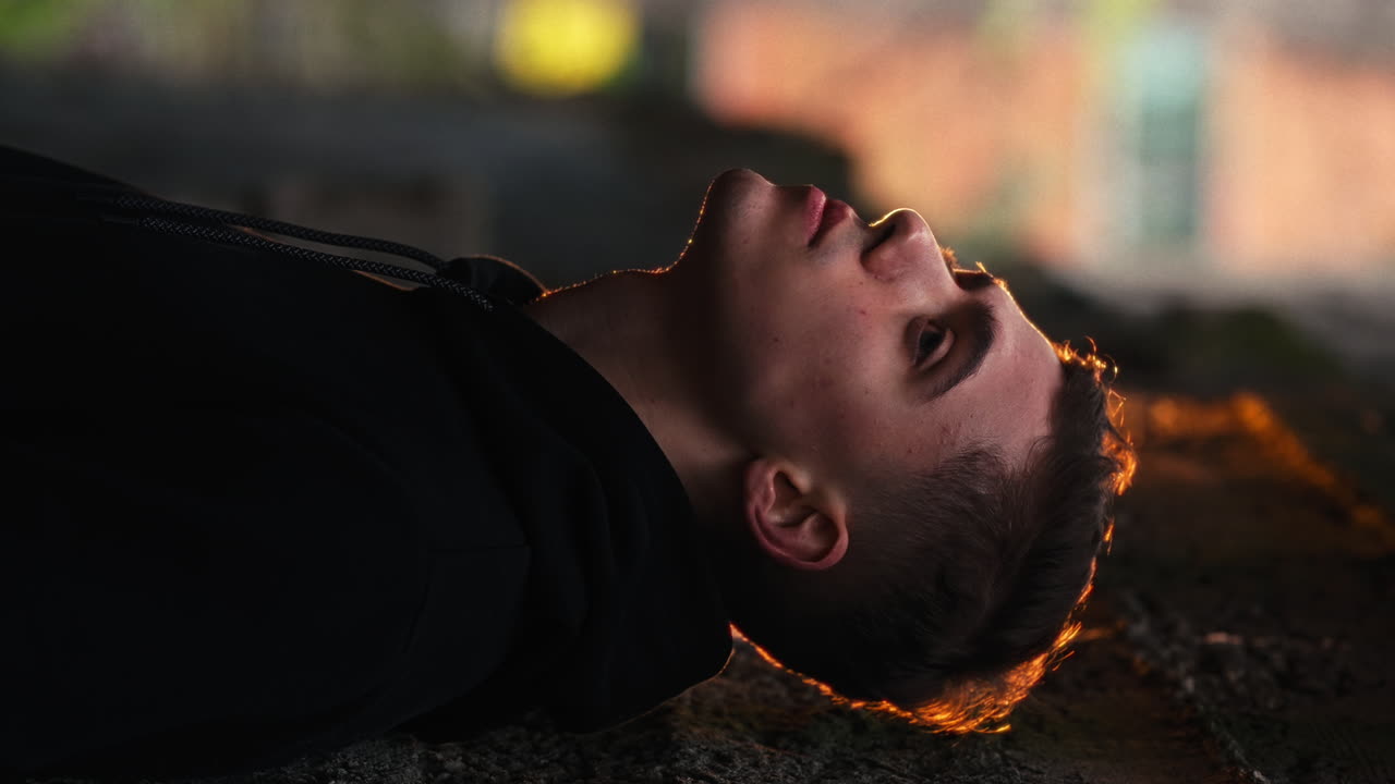 Vertikal video, portrett av en kjekk ung mannlig modell som lener seg mot en bymur ved solnedgang