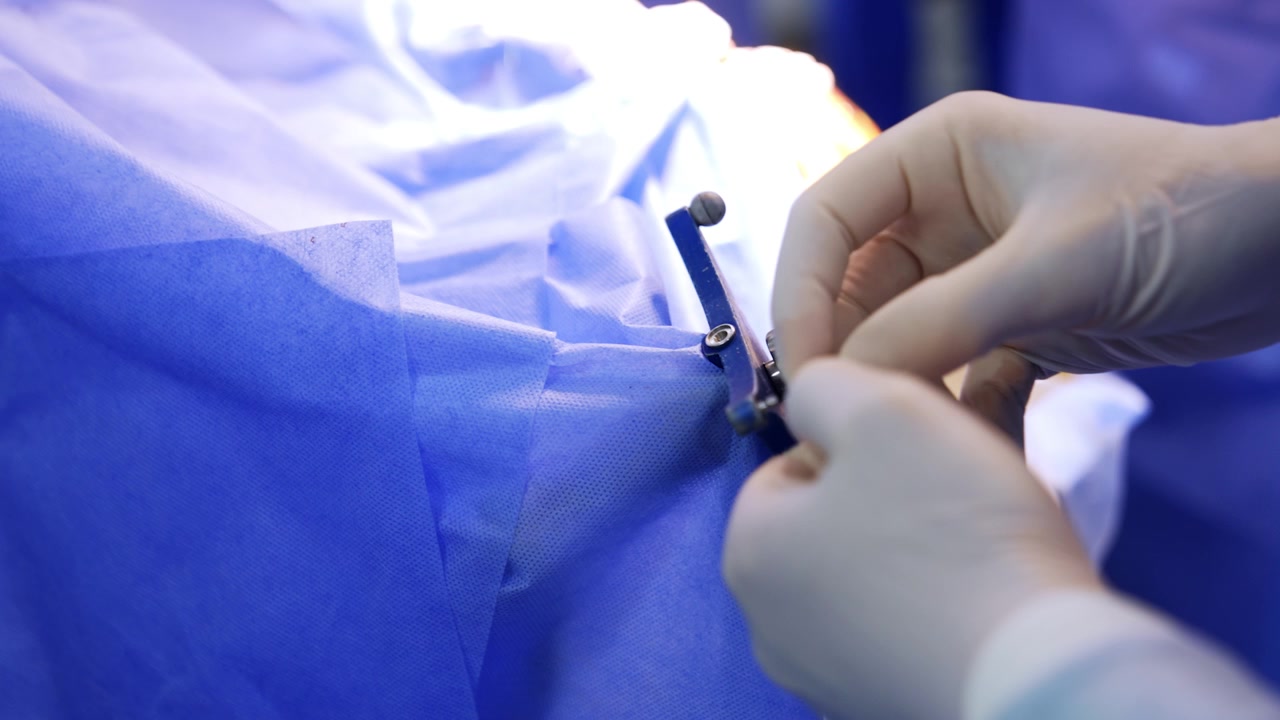 Mani del medico con guanti in lattice dispongono uno strumento per l'uso in un intervento neurochirurgico. Primo piano. Il paziente è coperto da un telo blu.