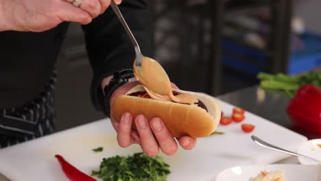 chef preparando un perrito caliente con salsa