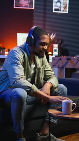 vertical video focused black guy teleworking on laptop in a living room feels happy