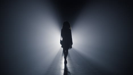 Silhouette-girl-walking-darkness.-Woman-going-straight-on-camera-dark-background