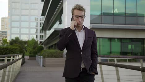 Serious-young-man-walking-outside,-talking-on-phone