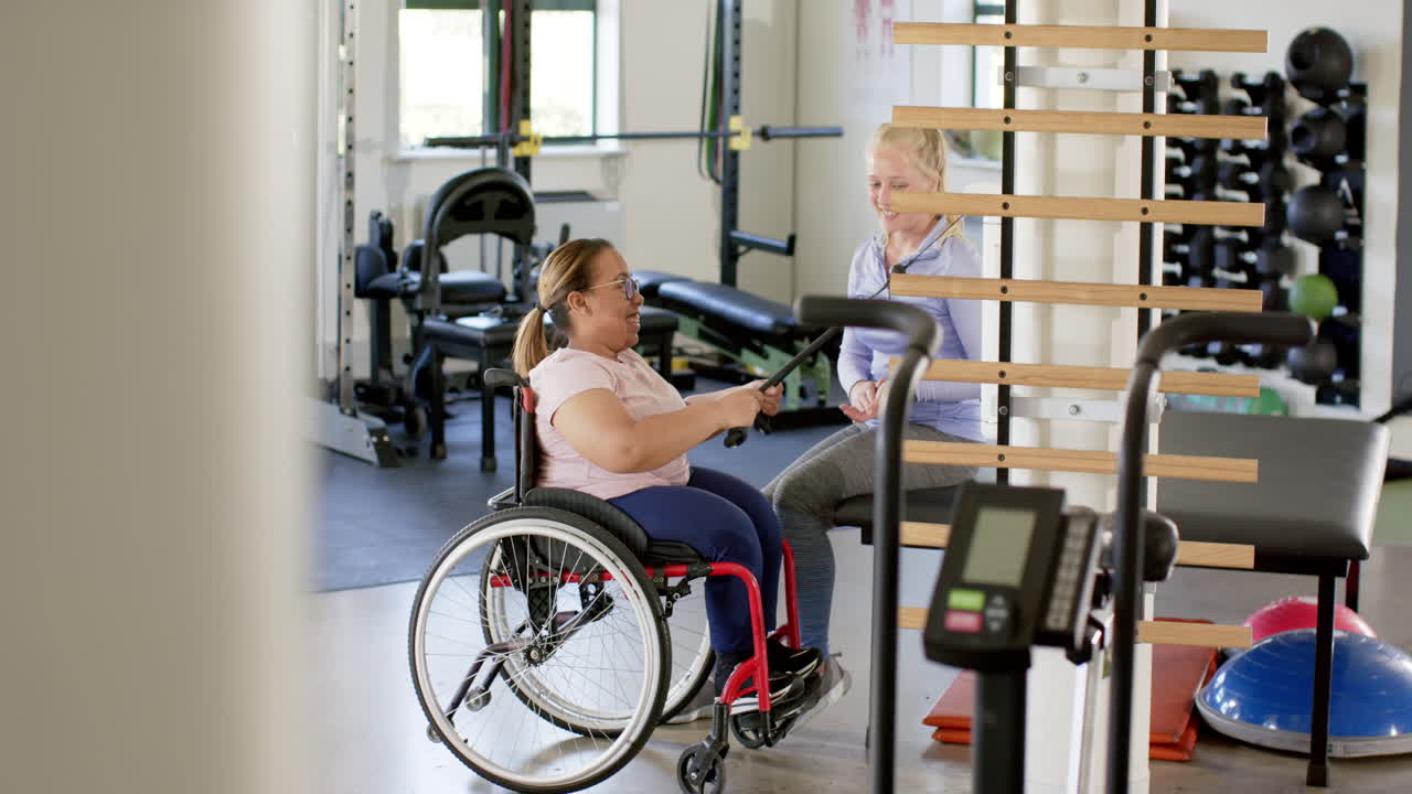 woman in wheelchair with paraplegia exercising with therapist in rehabilitation center gym