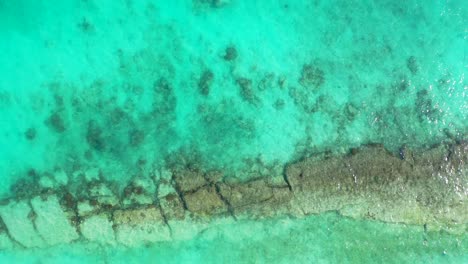 Beautiful-abstract-texture-from-turquoise-lagoon-surface-with-rocky-bottom-and-coral-reefs-thriving-through-white-sand,-copy-space