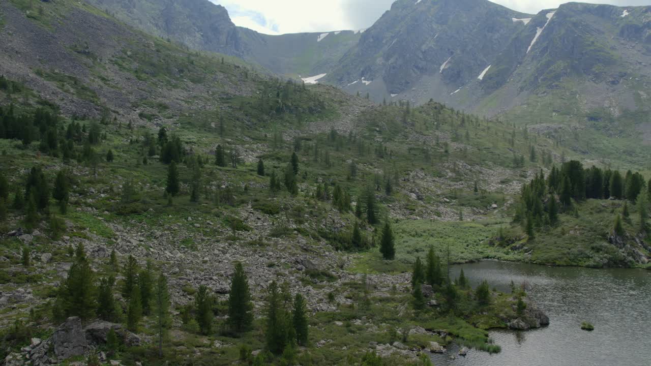 Vidt landskapsopptak av Karakol-sjøenes dal med steinete skråninger, alpin eng og barskog under en skyet himmel, Altai-republikken, Russland, et naturbilde fra sommerreise.