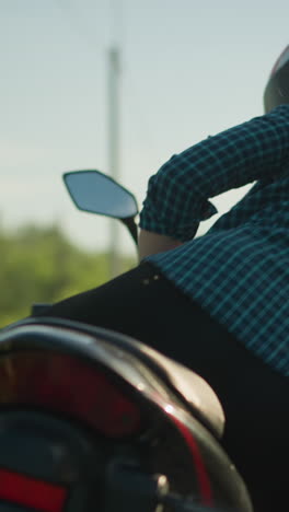 um close-up de um motociclista desmontando de uma motocicleta enquanto ela se afasta, com uma visão borrada de um carro com seus faróis em segundo plano, vindo da distância na estrada