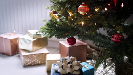 Tilt-shot-of-baubles-hanging-on-a-Christmas-tree-and-gifts-arranged-below,-close-up