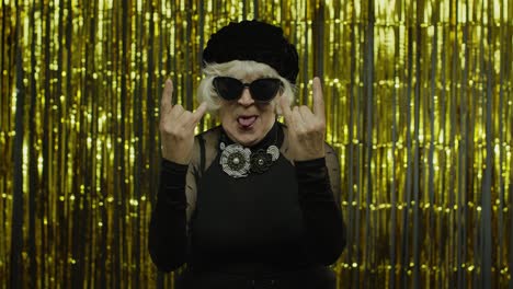 excited positive senior woman showing rock and roll gesture and sincerely smiling, showing tongue