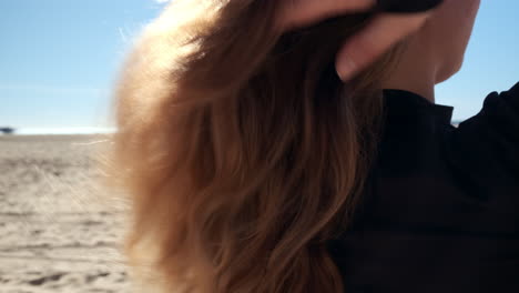 young blonde woman in a workout suit fixing her hair, on the beach of santa monica california