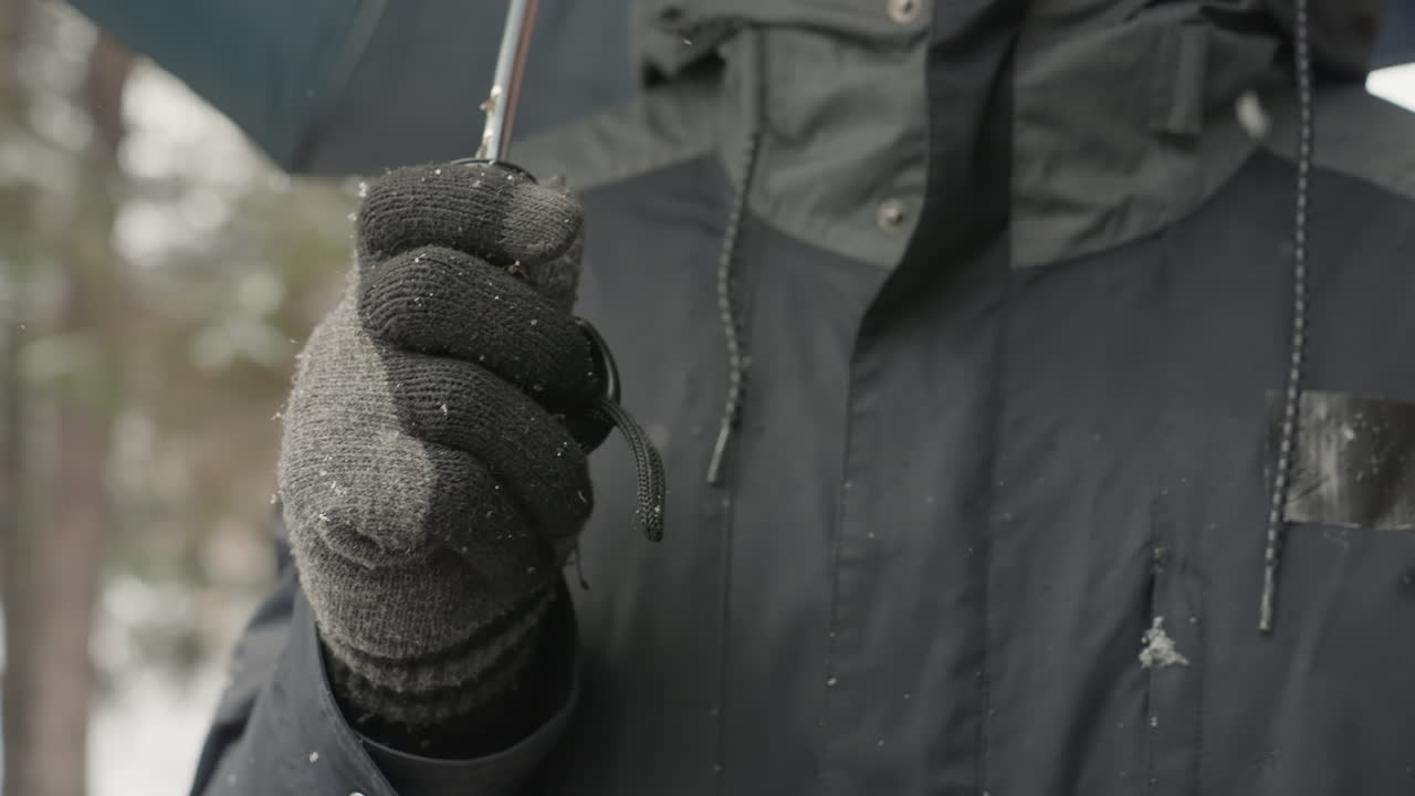 Sne smelter under varme handsker. Frosne vejrdetaljer fanget med let regn og hyggelig påklædning. Detaljeret udsigt over vintertøj midt i smeltende sne og blød skovbaggrundsbelysning