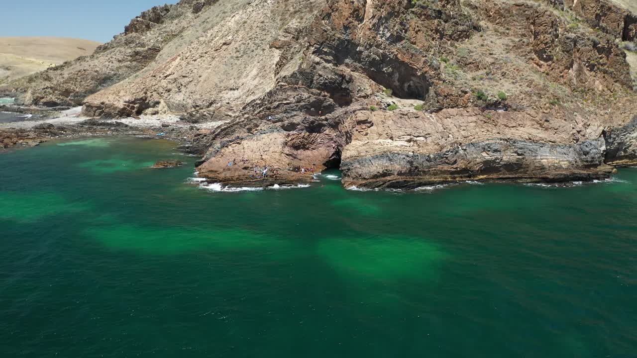 Ripresa con drone di un giovane che salta tra due scogliere, con altri turisti che osservano dal lato.