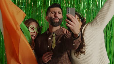 fotografía de estudio de amigos vestidos con novedades irlandesas y accesorios posando para selfies celebrando el día de san patricio contra un fondo de oropel verde 1