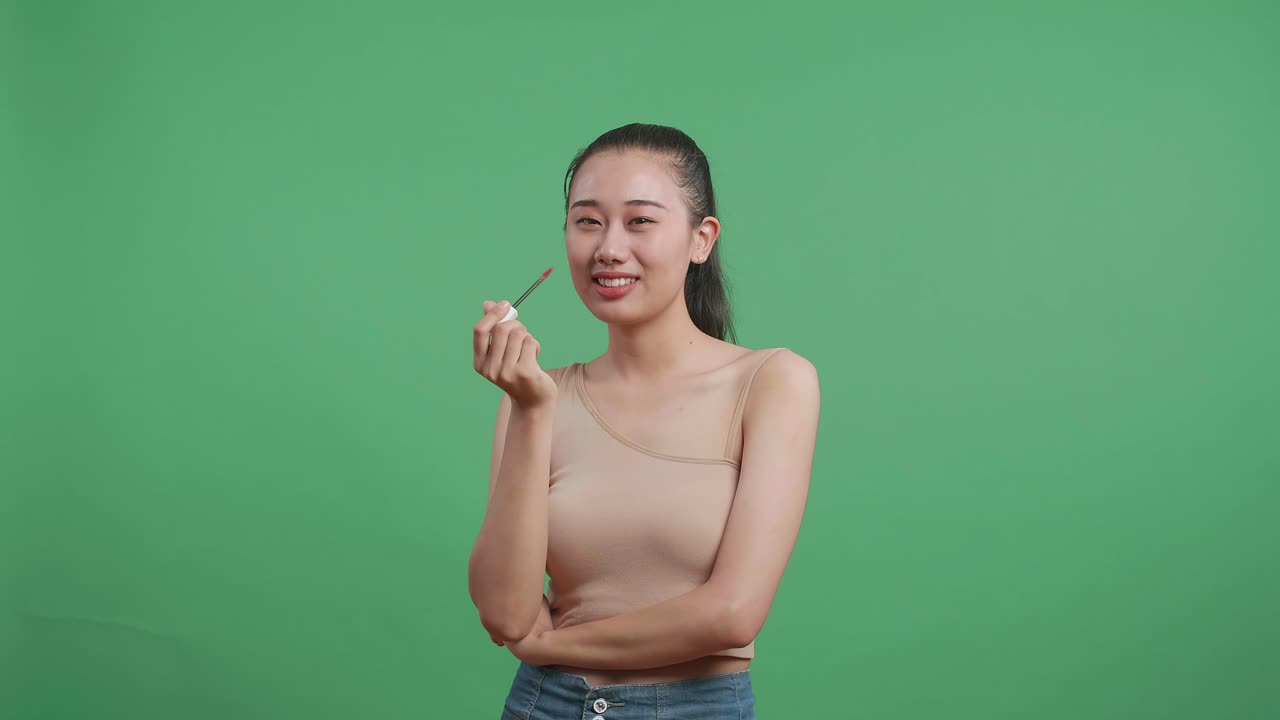 아시아 여성이 립스틱을 쓰고 스튜디오에서 녹색 화면 배경에 미소 짓는 동안 키스를 보내고 있습니다.