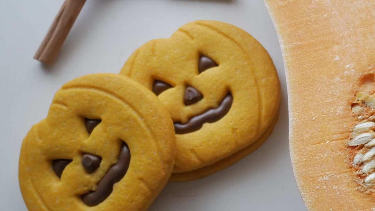 Biscotti Jack-o'-lantern accanto a una zucca fresca creano una festosa scena di preparazione di dolci per Halloween