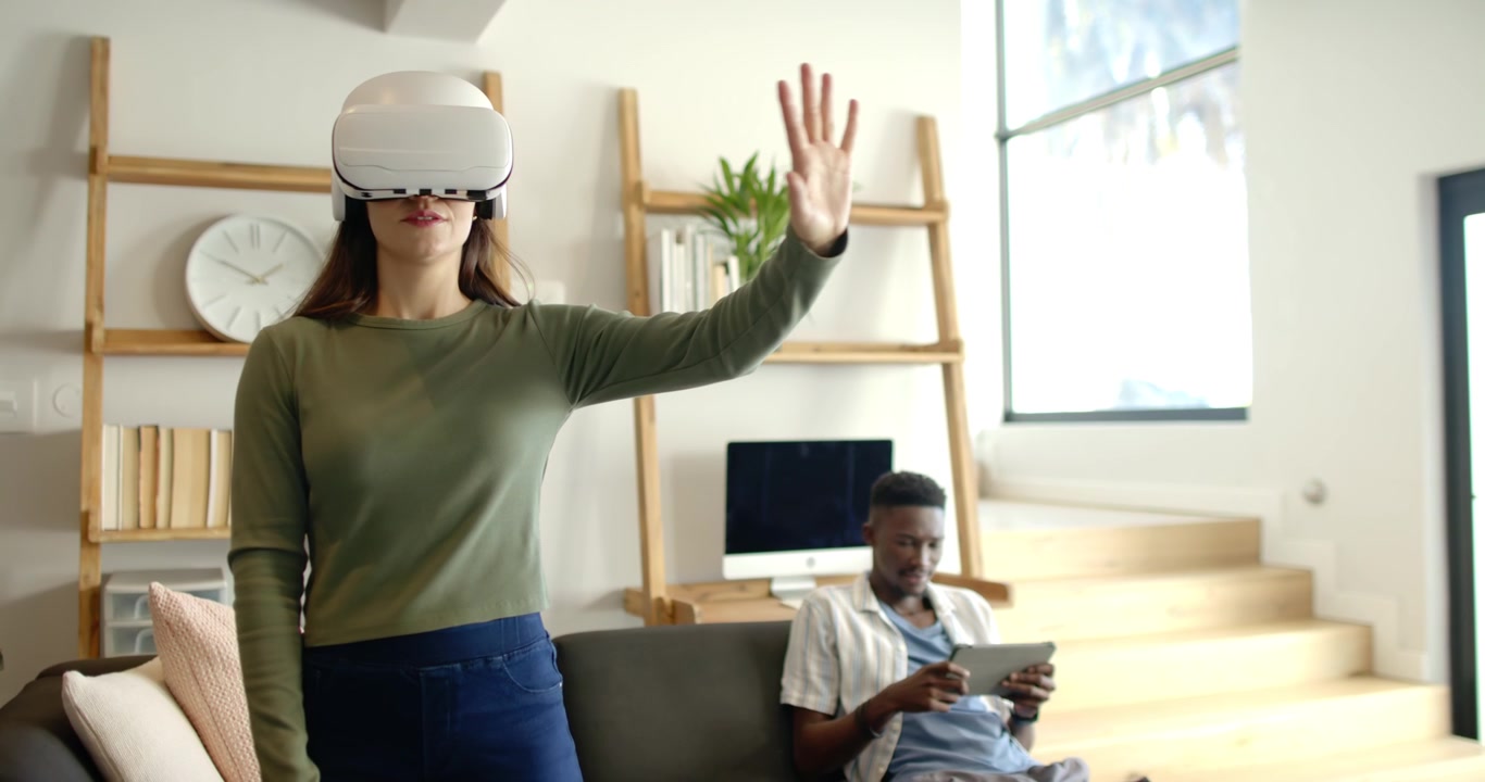 Ett mångkulturellt par i vardagsrummet, kvinnan bär ett VR-headset, startar och navigerar i VR, medan mannen använder en surfplatta.