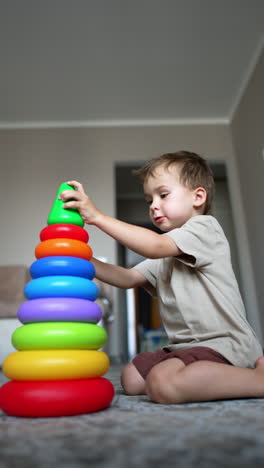 baby boy sits on the floor building a colorful pyramid. toddler kid turns the toy and disassembles it. low angle view. vertical video.
