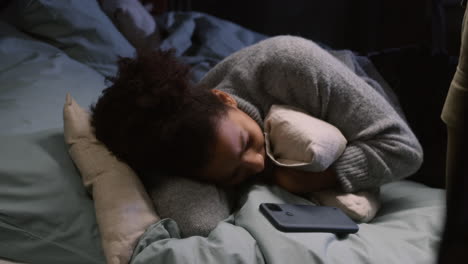 mujer joven abrazando almohada y acostada en el dormitorio