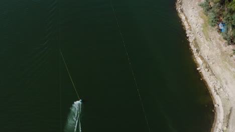 Bird's-Eye-View-Of-A-Water-Skier-Being-Pulled-By-A-Boat-On-The-Calm-Lake-In-Teleski-Water-Park-In-Vieira-Do-Minho,-Portugal---aerial-drone