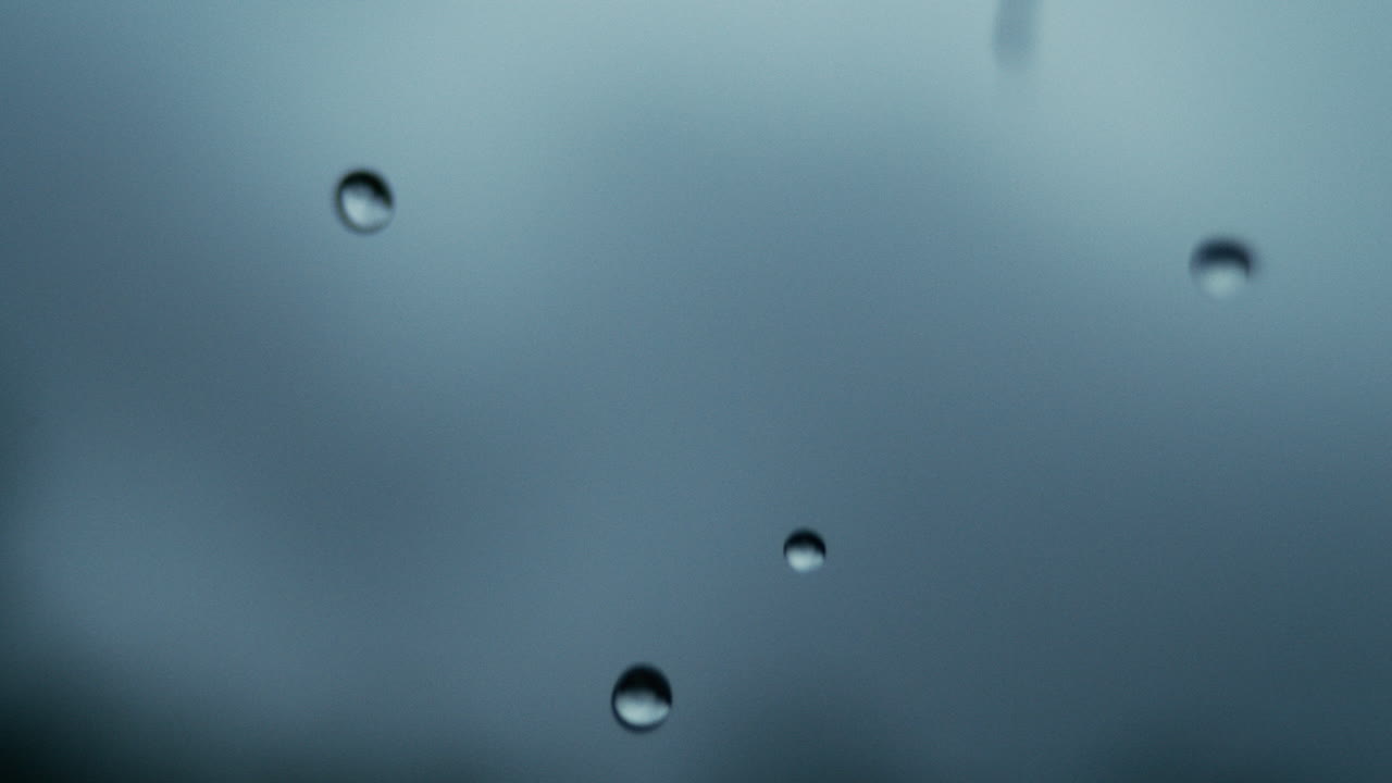 Water drops fall from smooth surface into dark pool in slow motion, macro closeup with depth of field