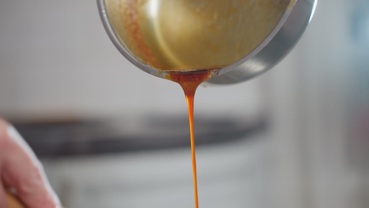 primer plano de una persona vertiendo sopa roja vibrante de una olla de metal mientras se agita en un cuenco blanco, el líquido rico fluye suavemente, mezclándose con los ingredientes a medida que las manos se mezclan cuidadosamente