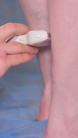a doctor with diagnostic equipment conducts an ultrasound examination of the patient’s leg veins.