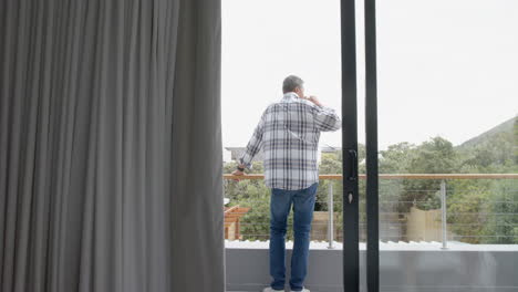 Senior-biracial-man-drinking-coffee-standing-on-balcony-at-home,-copy-space,-slow-motion