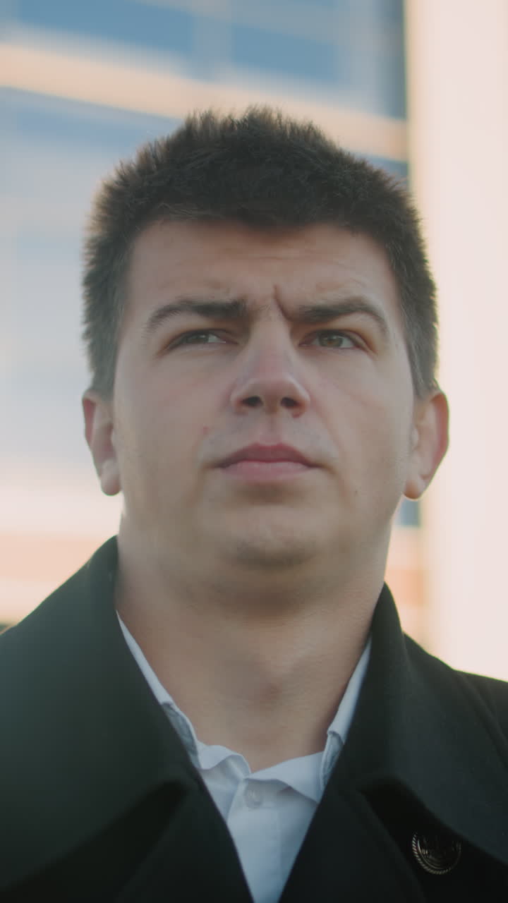 검은 옷을 입은 남자가 집중적이고 진지한 표정으로 목걸이를 조정합니다. 빛은 그의 특징을 강조합니다. 유리 건물 배경에 서서 결단력을 묘사합니다.