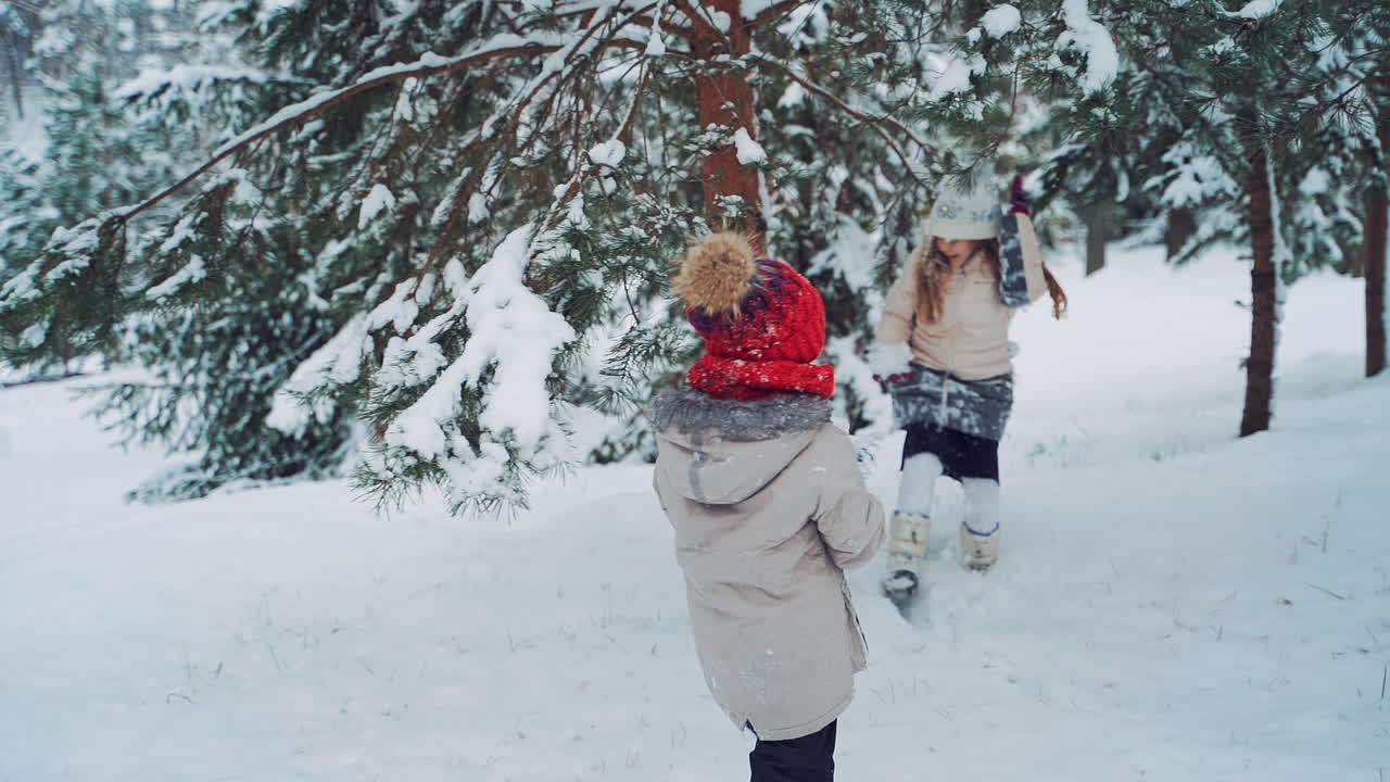 Happy children are playing in the forest in winter. Snowy background outdoors and two little girls spending a great time together. Slow motion.