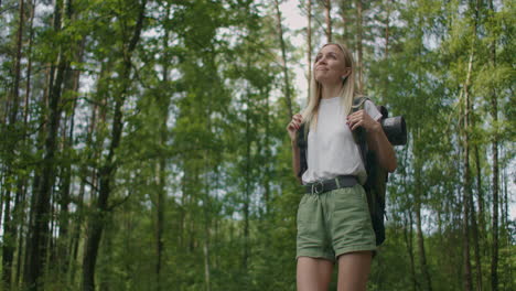 slow motion: adult caucasian woman wearing shorts and t-shirt hikes through woods. female hiker with backpack walking