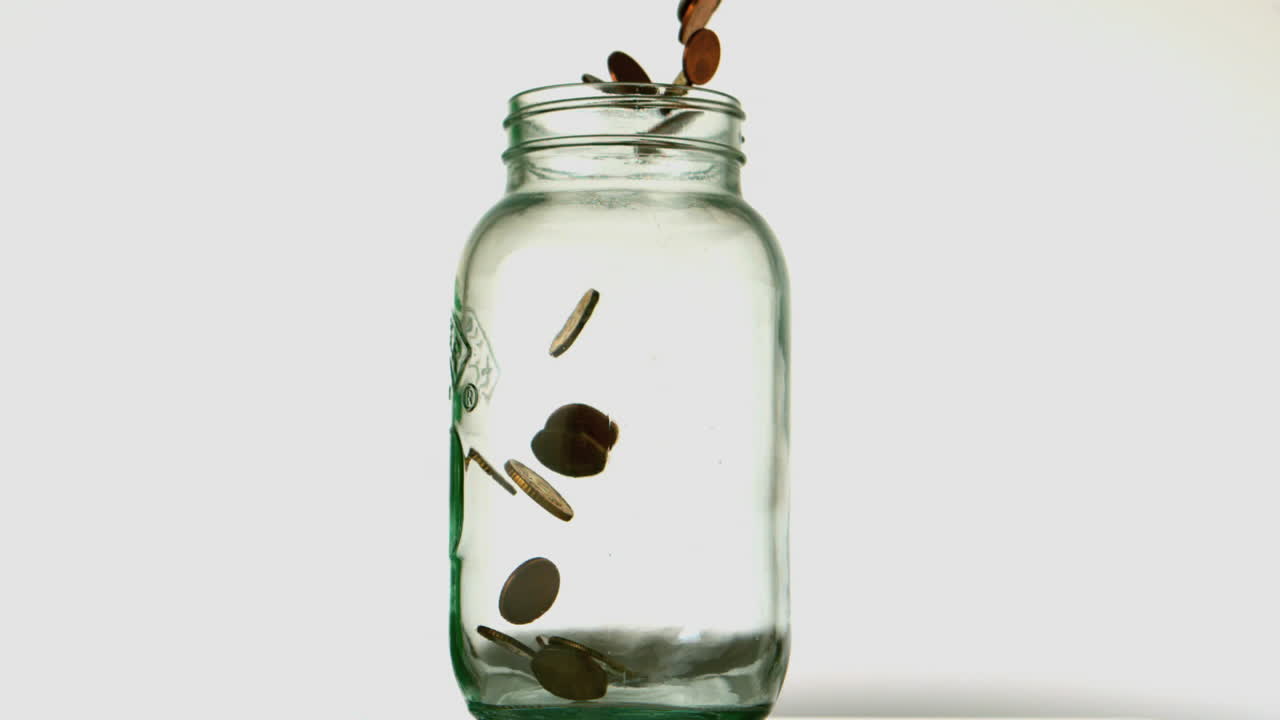 Coins pouring into glass jar on white background