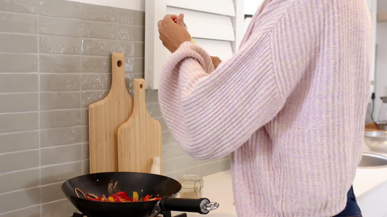 Cooking stir-fry vegetables, woman in kitchen wearing cozy sweater, focused on task