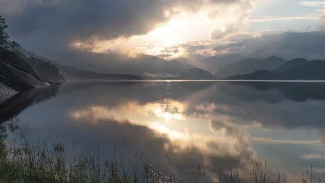 Beautiful-sunset-skies-reflected-in-the-still-mirrorlike-waters-of-the-lake-with-rocky-banks