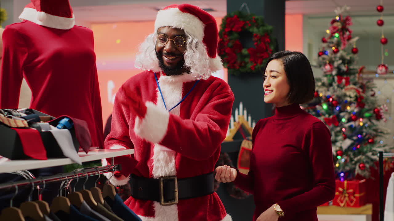 asistente minorista actuando como santa claus ayudando al cliente en la tienda de compras a encontrar la blusa roja necesaria para el atuendo de la fiesta de navidad. empleado ayudando a una mujer en una tienda de moda durante la temporada de ventas de navidad