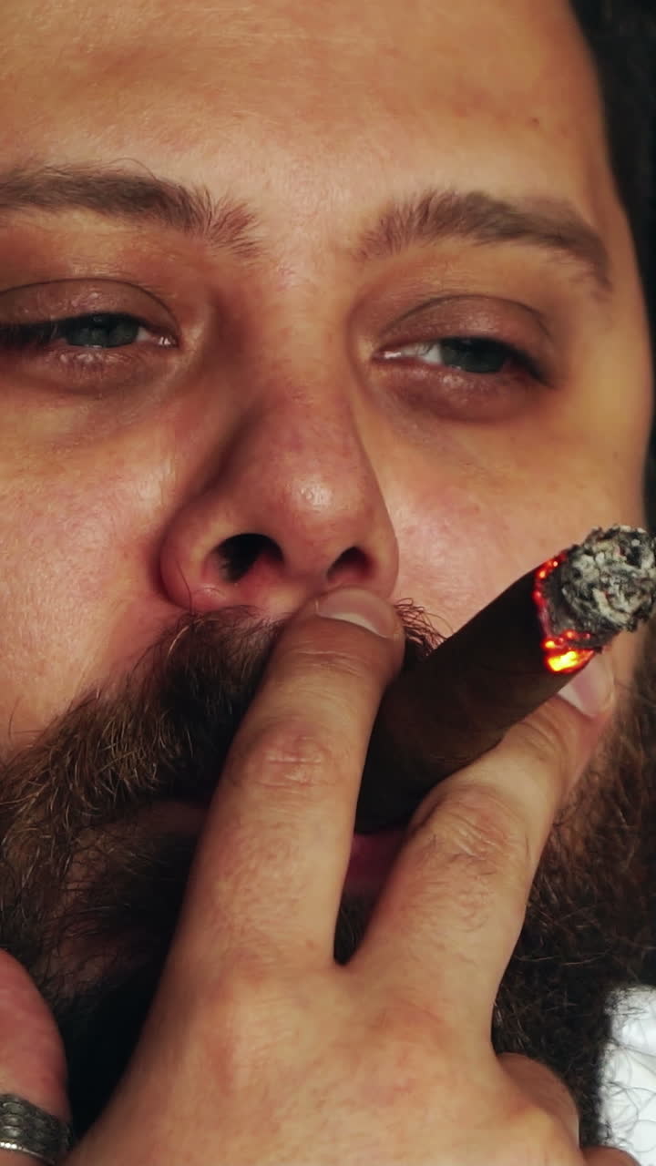 Brutal serious man in studio. Brutal caucasian serious hipster sitting and smoking cigar