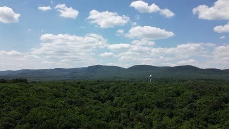 Aerial-hyperlapse-of-clouds-on-a-sunny-day---approaching-the-hills-of-Börzsöny,-Hungary---water-tower-sphere-in-the-forest