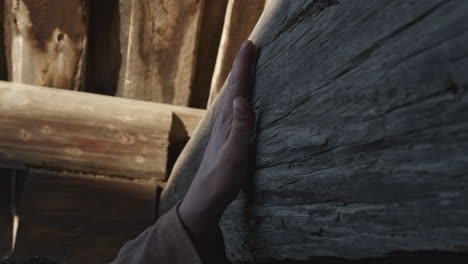 hand touching a weathered wooden beam in a log cabin interior