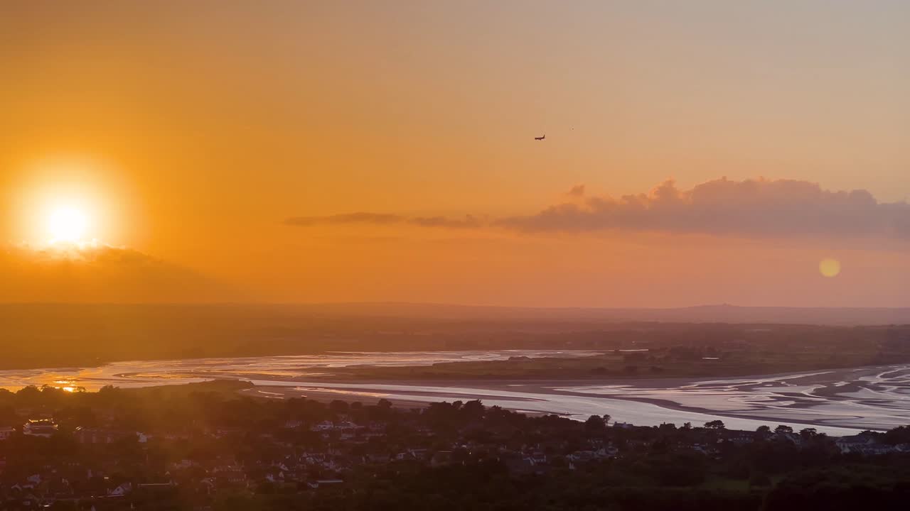 Sunset silhouette of an airplane flying toward glowing orange horizon over darkened landscape