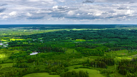 a dynamic aerial hyperlapse flies sideways at high speed over a vast and beautiful latvian landscape, revealing a patchwork of green forests, fields, and pristine lakes