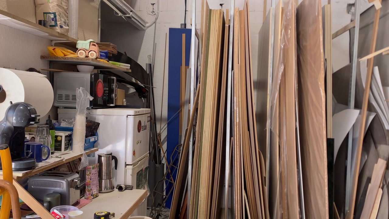 Ripostiglio disordinato con pannelli di legno impilati, scaffali che contengono macchina da caffè, tostapane, asciugamani di carta e forniture da cucina