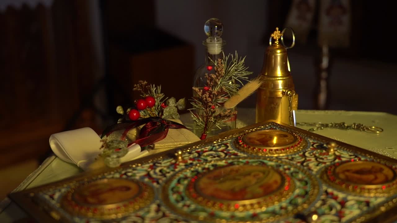 A Bible lies open on a wooden table surrounded by baptism items, including a small bowl, candles, and a cloth