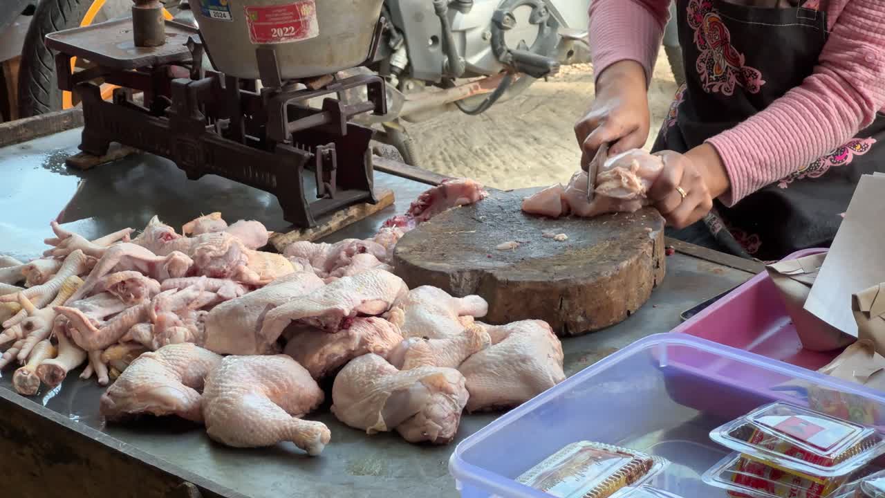 The hands of a chicken meat seller cutting a whole chicken with a knife and wooden chopping board at a traditional Indonesian market